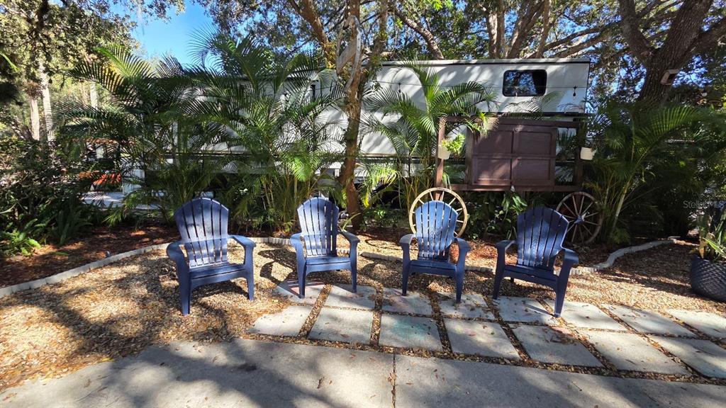 Four blue Adirondack chairs sit on a stone patio in front of a parked trailer — 174 APPALOOSA TRAIL, RIVER RANCH, FL