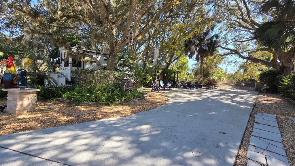 A concrete driveway leads to a recreational vehicle parked under large, mature oak trees — 174 APPALOOSA TRAIL, RIVER RANCH, FL