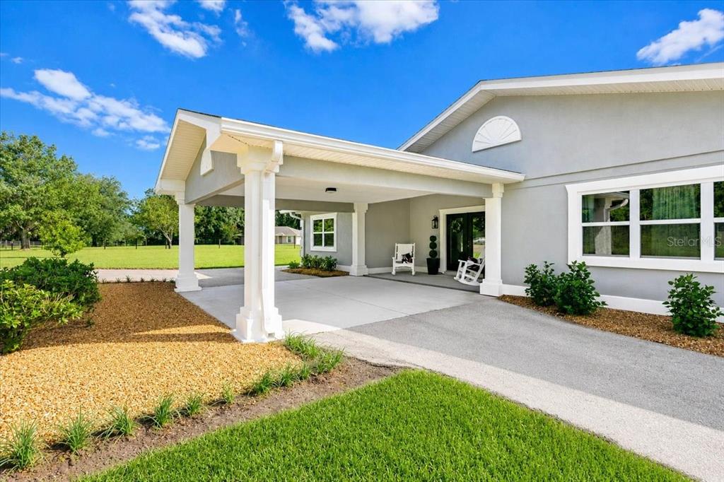 A gray house exterior features a covered carport with white columns and a concrete driveway — 26013 N COUNTY ROAD 1491, ALACHUA, FL