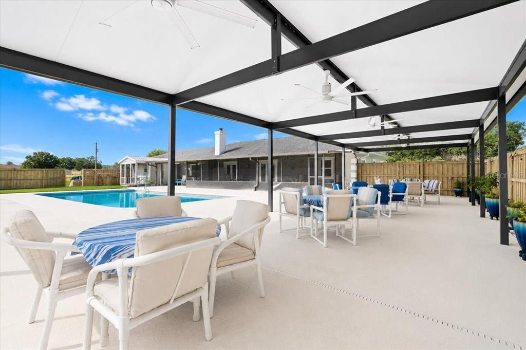 A covered patio features a swimming pool, outdoor dining sets, and a white concrete deck — 26013 N COUNTY ROAD 1491, ALACHUA, FL