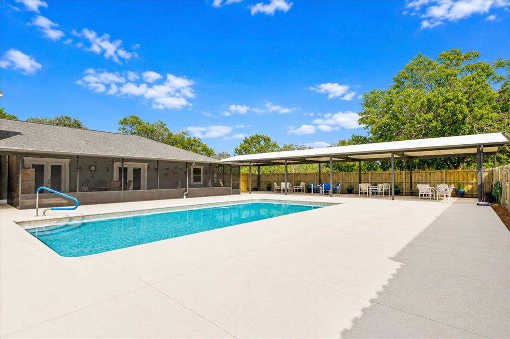A rectangular swimming pool sits on a concrete patio next to a covered outdoor seating area — 26013 N COUNTY ROAD 1491, ALACHUA, FL