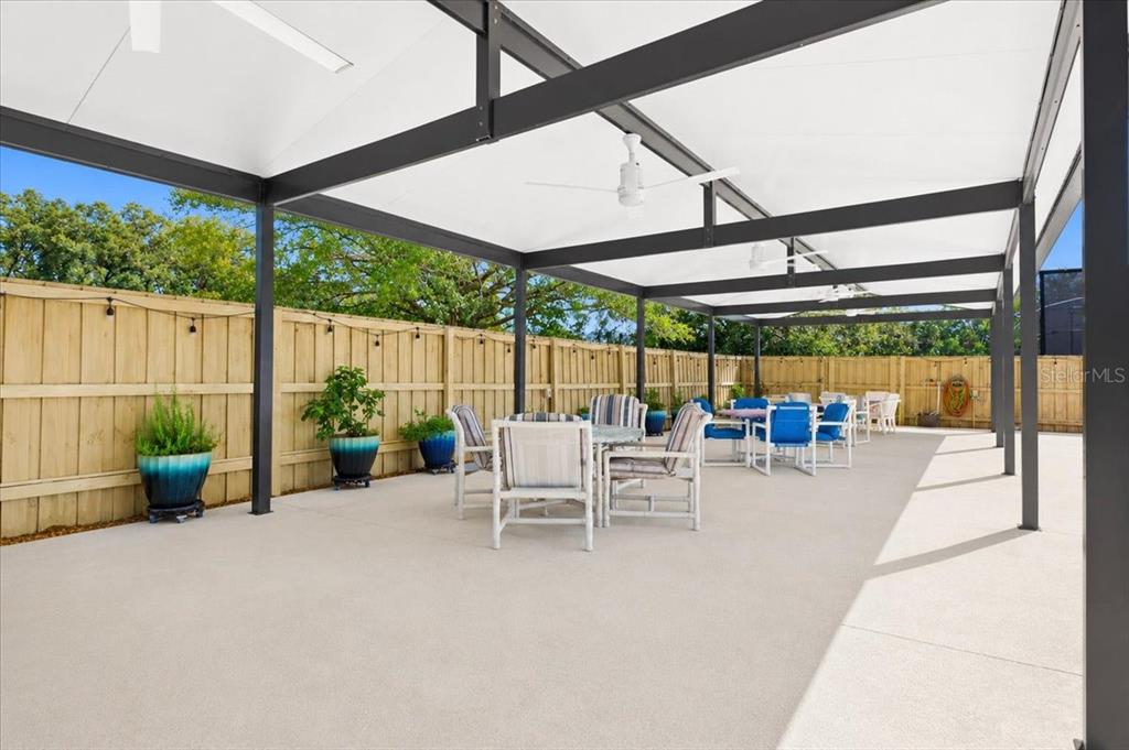 A covered outdoor patio features a concrete floor, metal frame, ceiling fans, and wooden fencing — 26013 N COUNTY ROAD 1491, ALACHUA, FL