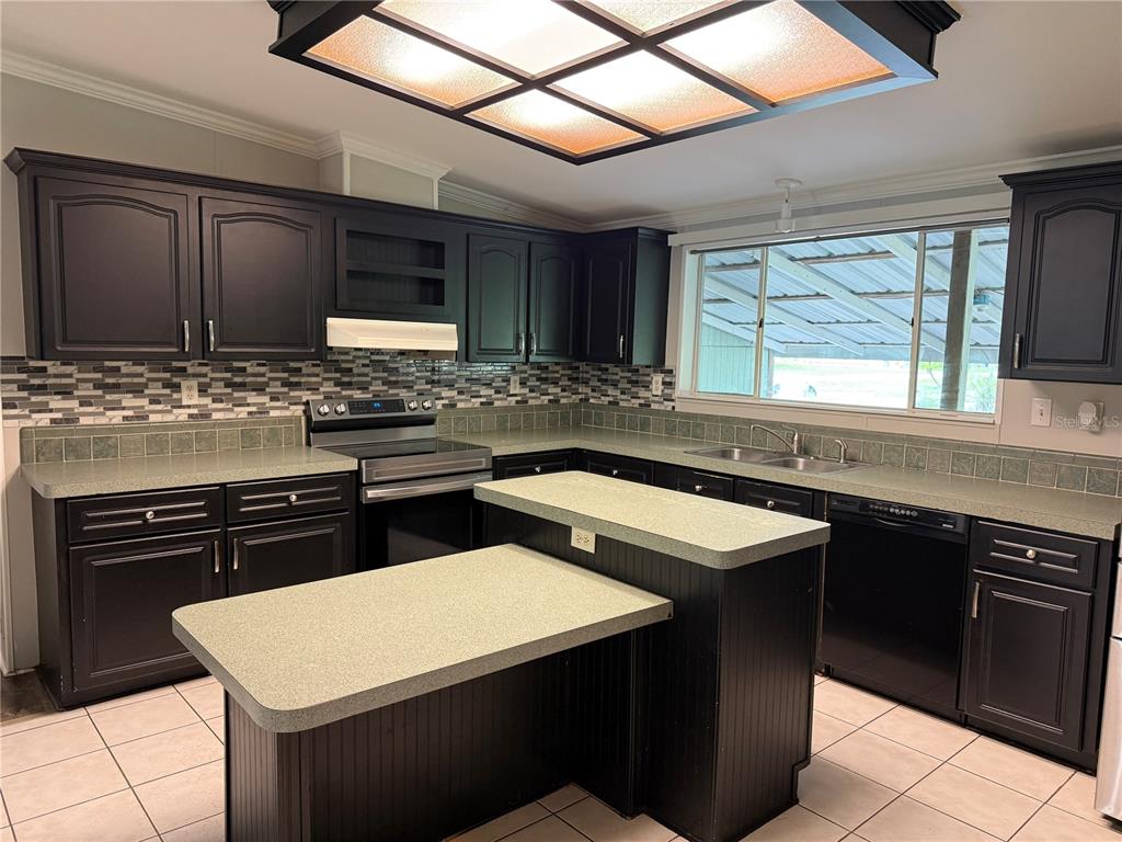A kitchen features dark cabinets, a tiered island, tiled countertops, and a large ceiling light — 3704 GARON AVENUE, RUSKIN, FL