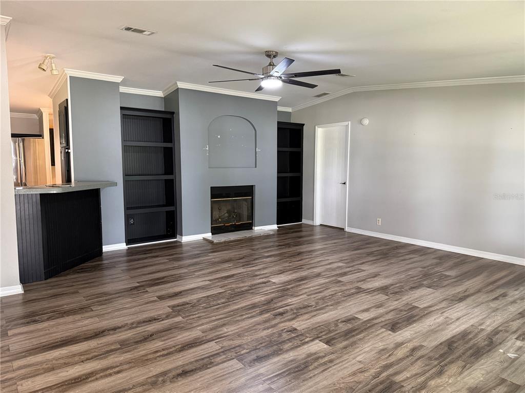 A living room features wood-look flooring, a fireplace with built-in shelving, and a ceiling fan — 3704 GARON AVENUE, RUSKIN, FL