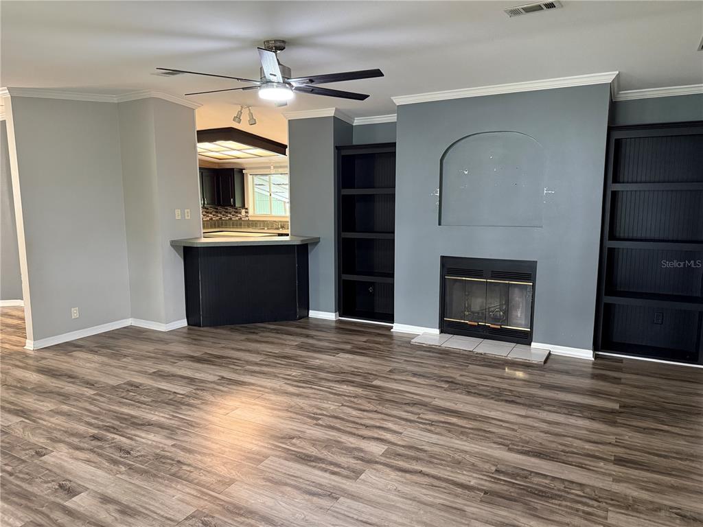 A living room features wood-look flooring, a fireplace with built-in shelves, and an adjacent kitchen — 3704 GARON AVENUE, RUSKIN, FL