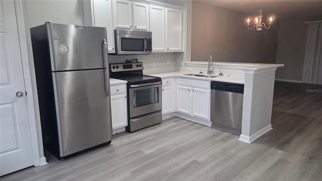 A kitchen with white cabinets, stainless steel appliances, and light wood-look flooring — 4439 SW 49TH AVENUE, OCALA, FL