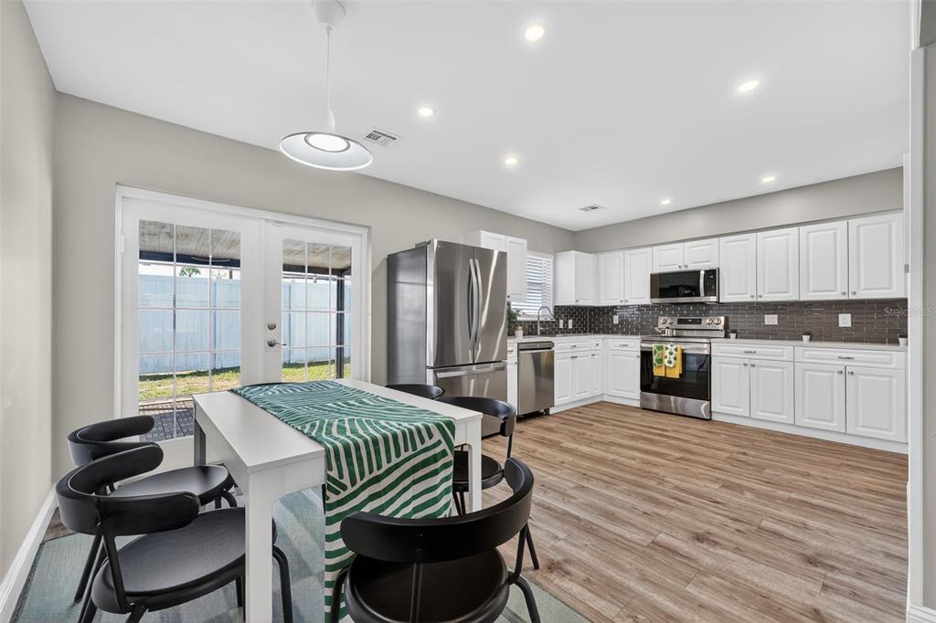A kitchen with white cabinets, stainless steel appliances, and a dining table near glass doors — 2806 UPPER TANGELO DRIVE, SARASOTA, FL