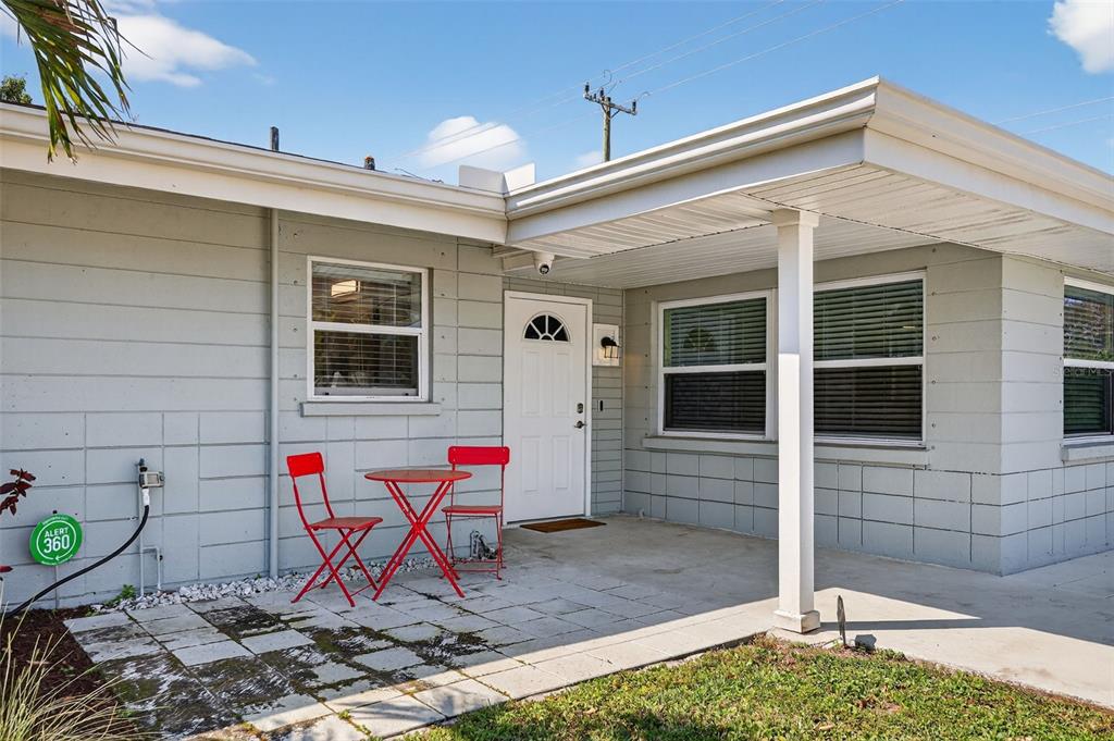 A gray concrete block house exterior features a covered porch, white door, and red furniture — 2806 UPPER TANGELO DRIVE, SARASOTA, FL