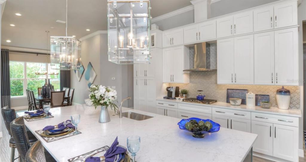 A modern kitchen features white cabinetry, a large quartz island, and glass pendant lighting — 9 NEWCASTLE LANE, ORMOND BEACH, FL