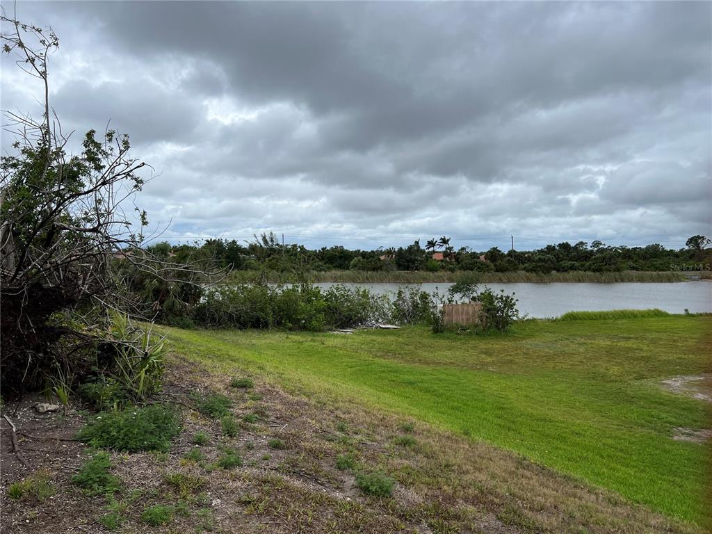 A grassy yard slopes down toward a lake under a cloudy sky — WOODBRIDGE DRIVE, VENICE, FL
