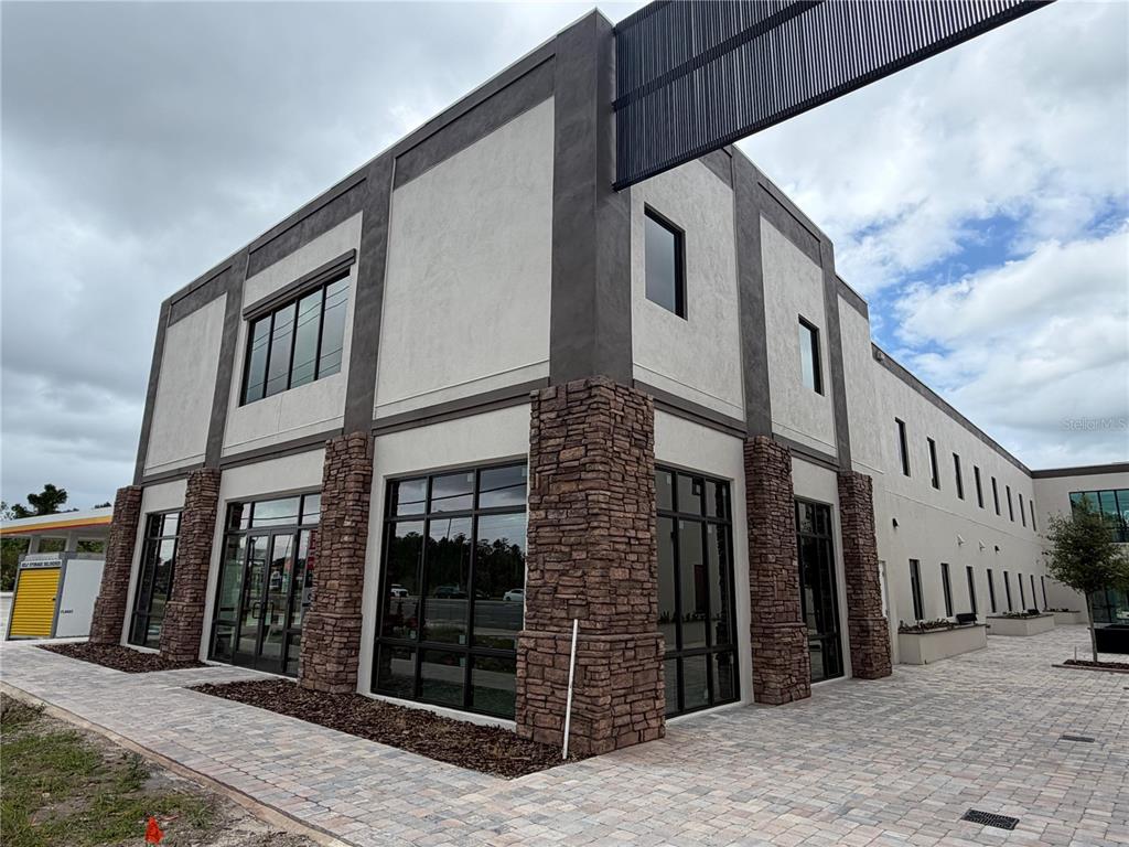A modern two-story commercial building features stone-clad pillars, large glass windows, and stucco walls — 4560 W IRLO BRONSON MEMORIAL HIGHWAY UNIT A, KISSIMMEE, FL