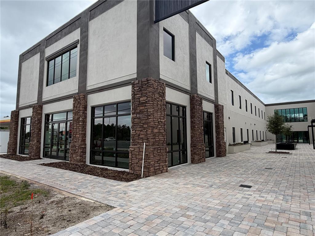 A modern commercial building exterior features stone pillars, large glass windows, and paved walkways — 4560 W IRLO BRONSON MEMORIAL HIGHWAY UNIT A, KISSIMMEE, FL