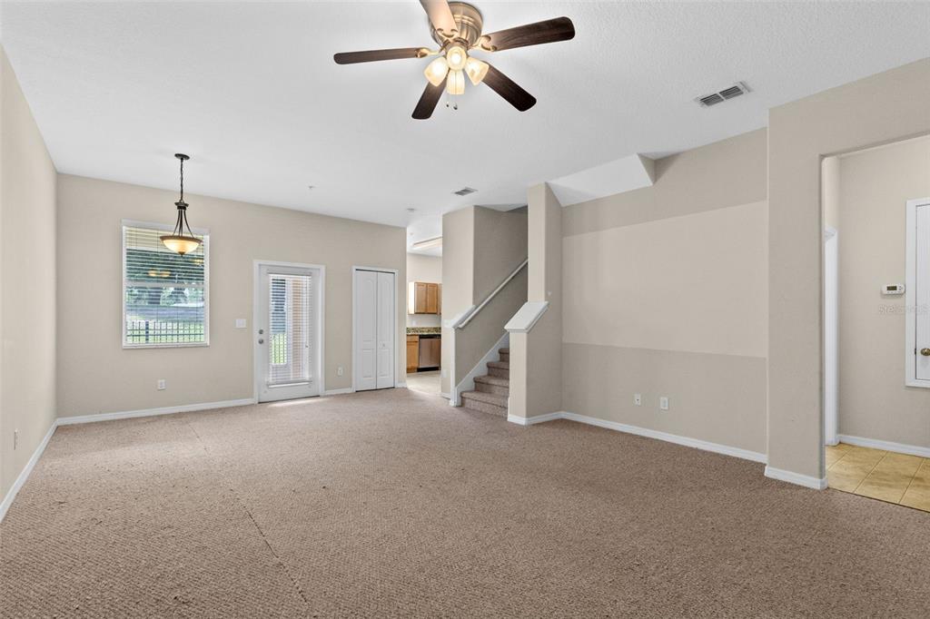 A carpeted living room features a ceiling fan, a staircase, and a sliding glass door — 1327 PRIORY CIRCLE UNIT 1327, WINTER GARDEN, FL