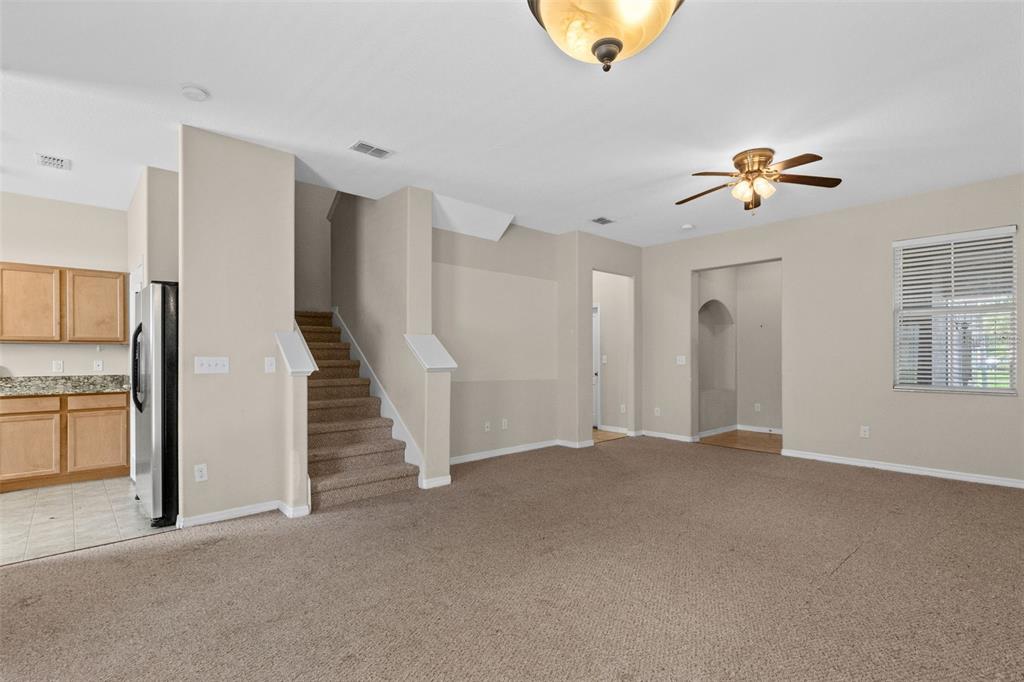A carpeted living room features a staircase, a ceiling fan, and an adjacent kitchen area — 1327 PRIORY CIRCLE UNIT 1327, WINTER GARDEN, FL