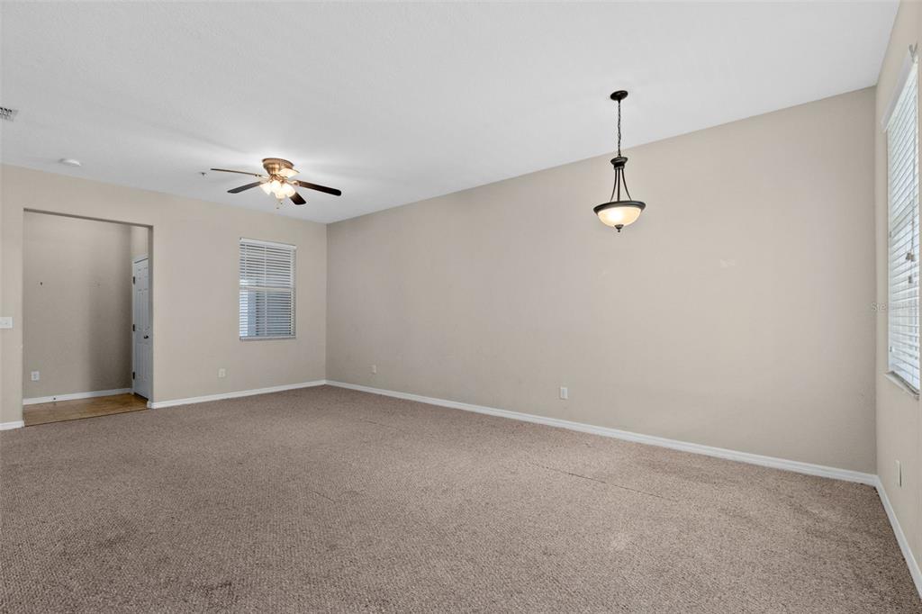 An empty living room with beige walls, tan carpeting, a ceiling fan, and a pendant light — 1327 PRIORY CIRCLE UNIT 1327, WINTER GARDEN, FL