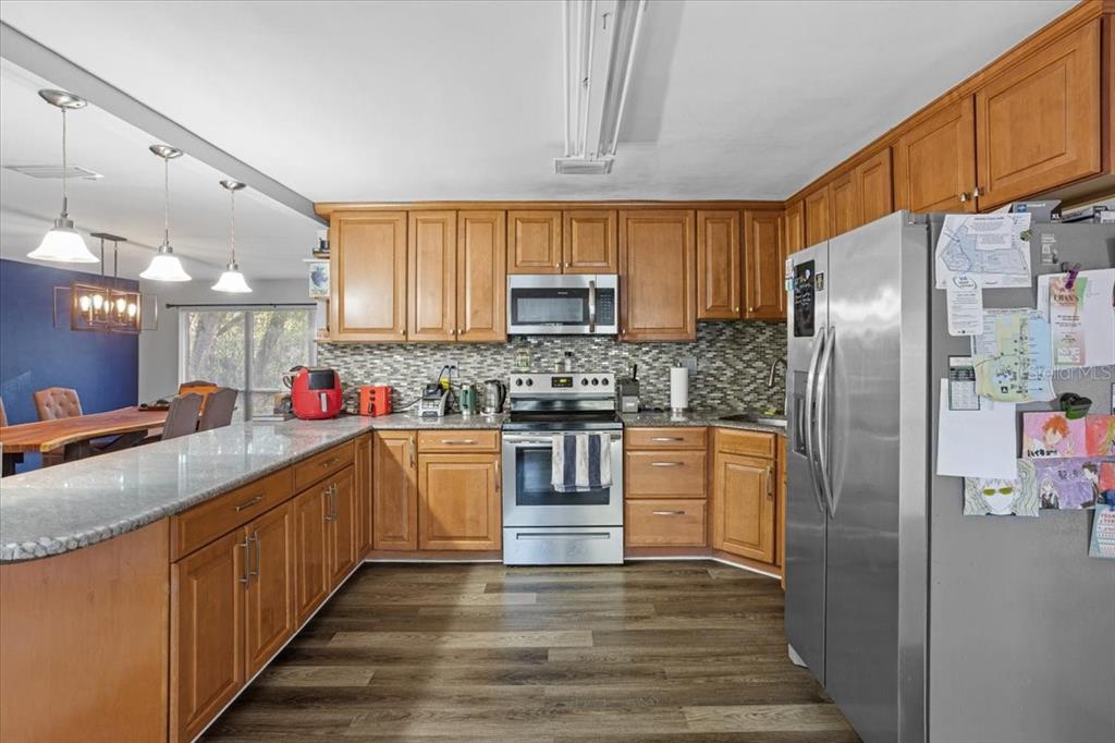 A kitchen with wood cabinets, stainless steel appliances, granite countertops, and wood-look flooring — 425 NW 79TH DRIVE, GAINESVILLE, FL