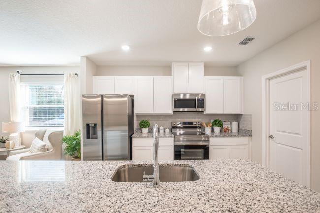 A kitchen features white cabinets, stainless steel appliances, and a granite-topped island with a sink — 12003 ROBINA ROAD, WEEKI WACHEE, FL