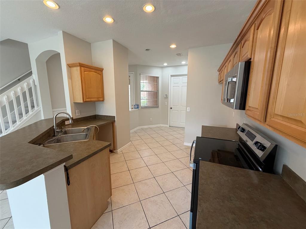 A kitchen features light wood cabinets, dark countertops, tile flooring, and a stainless steel microwave — 7530 CRANES CREEK COURT, WINTER PARK, FL