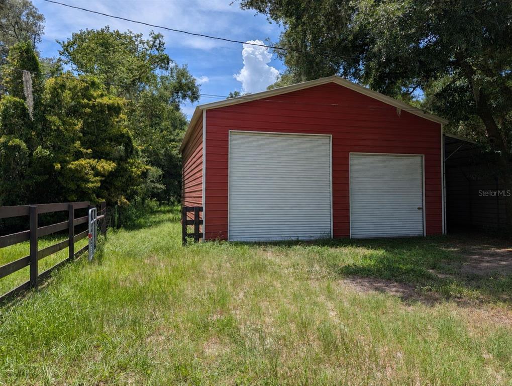 A red metal garage with two roll-up doors sits on a grassy lot with fencing — 876 SHAW LAKE ROAD, PIERSON, FL