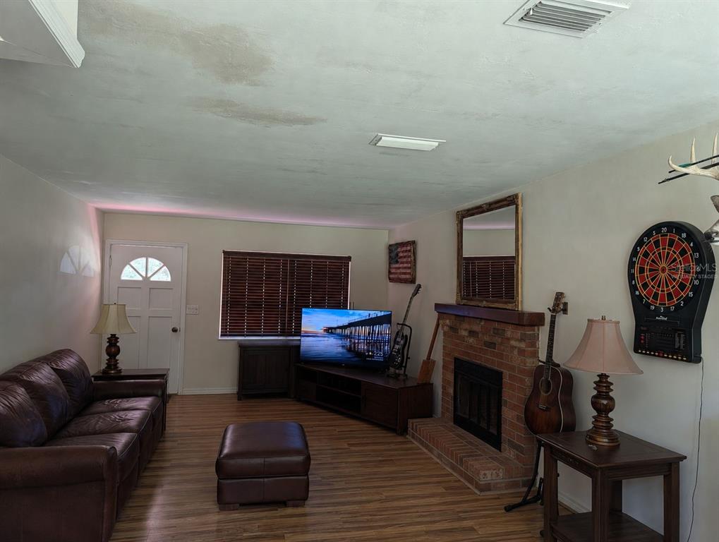 A living room features a brick fireplace, a leather sofa, a dartboard, and wood flooring — 876 SHAW LAKE ROAD, PIERSON, FL