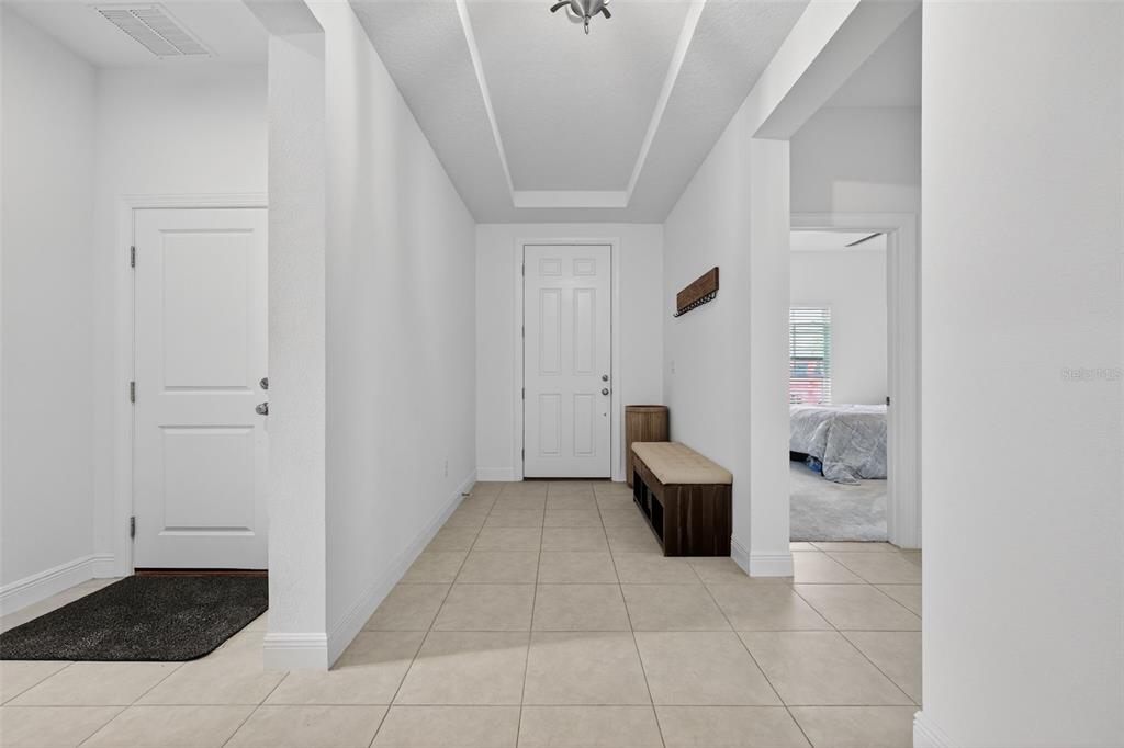 A bright entryway features light tile flooring, a white front door, and a wooden bench — 11912 RICHMOND TRAIL, PARRISH, FL
