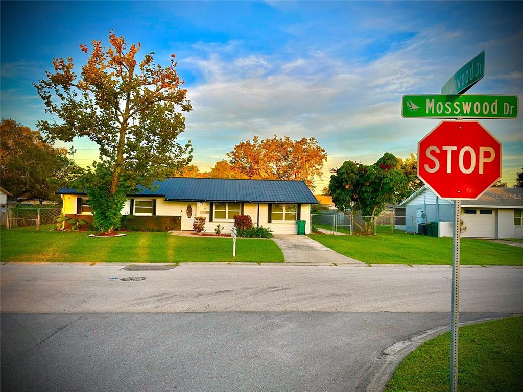 A single-story house with a blue metal roof sits behind a stop sign at an intersection — 1987 MOSSWOOD DRIVE, MELBOURNE, FL