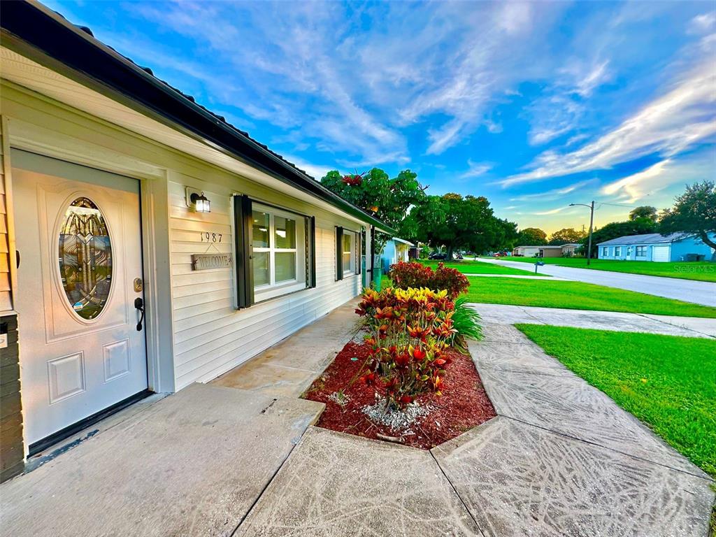 A white house exterior features a front door with an oval window and landscaped garden — 1987 MOSSWOOD DRIVE, MELBOURNE, FL