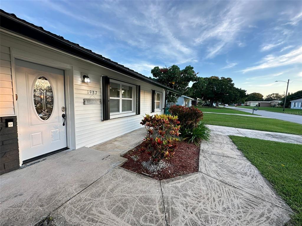 A white house exterior features a front door, a window, and a landscaped garden bed — 1987 MOSSWOOD DRIVE, MELBOURNE, FL