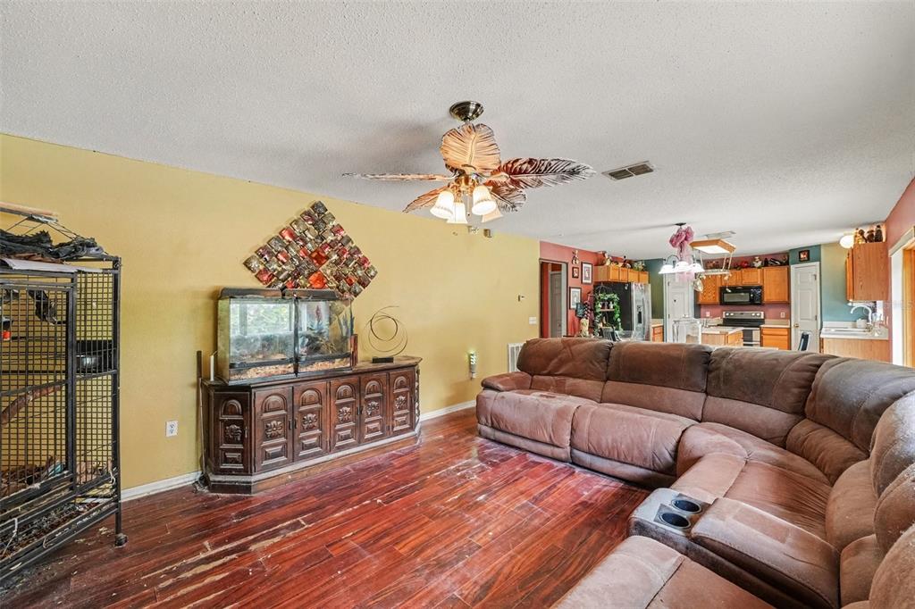 A living room with wood-look flooring, a brown sectional sofa, and a ceiling fan — 5888 WINDRIDGE DRIVE, WINTER HAVEN, FL