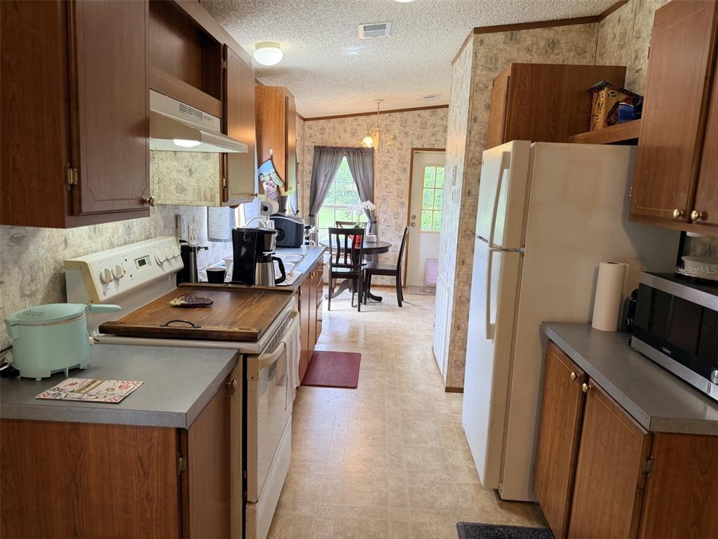 A kitchen with wood cabinets, laminate countertops, white appliances, and a small dining area — 230 E RODGERS BOULEVARD, CHIEFLAND, FL