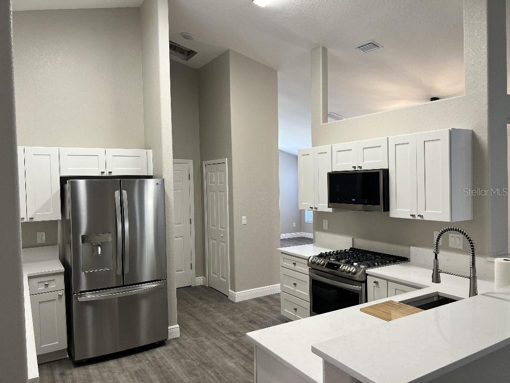 A kitchen features white cabinets, stainless steel appliances, and light countertops with gray flooring — 735 HURLEY DRIVE, WINTER GARDEN, FL