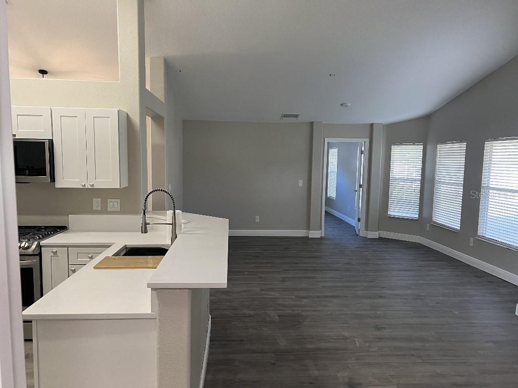 A kitchen with white cabinets and a breakfast bar opens into a spacious living area — 735 HURLEY DRIVE, WINTER GARDEN, FL