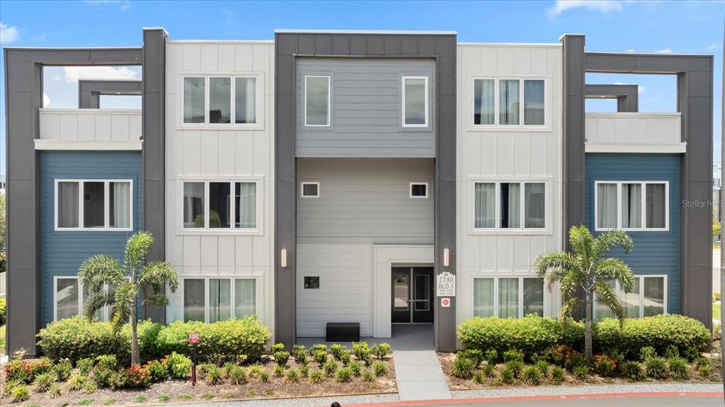 A three-story apartment building features a modern exterior with gray, white, and blue siding — 7740 SANDY RIDGE DRIVE UNIT 112, REUNION, FL