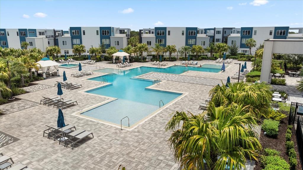 An outdoor swimming pool with lounge chairs and umbrellas sits in front of apartment buildings — 7740 SANDY RIDGE DRIVE UNIT 112, REUNION, FL