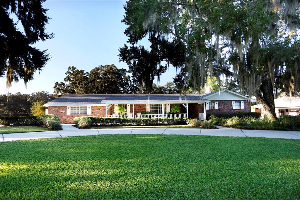 A single-story brick house with a covered front porch sits behind a large green lawn — 23378 EPPLEY DRIVE, BROOKSVILLE, FL