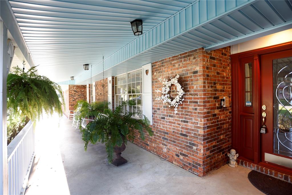 A covered brick porch features a red front door, hanging ferns, and white rocking chairs — 23378 EPPLEY DRIVE, BROOKSVILLE, FL