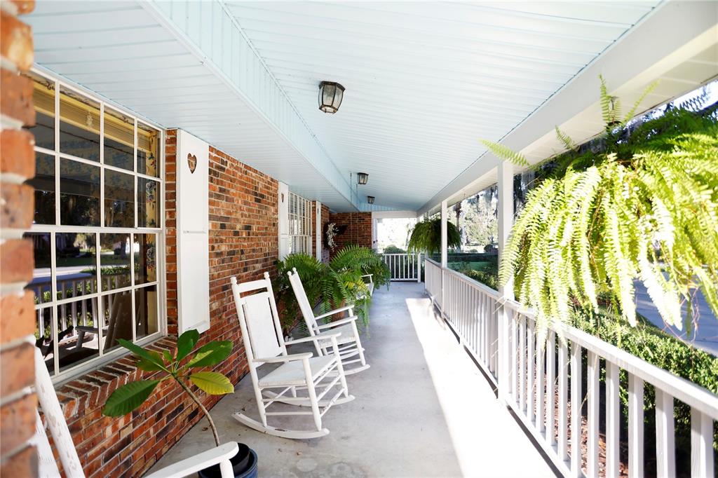 A long, covered brick porch features white rocking chairs, hanging ferns, and a white railing — 23378 EPPLEY DRIVE, BROOKSVILLE, FL