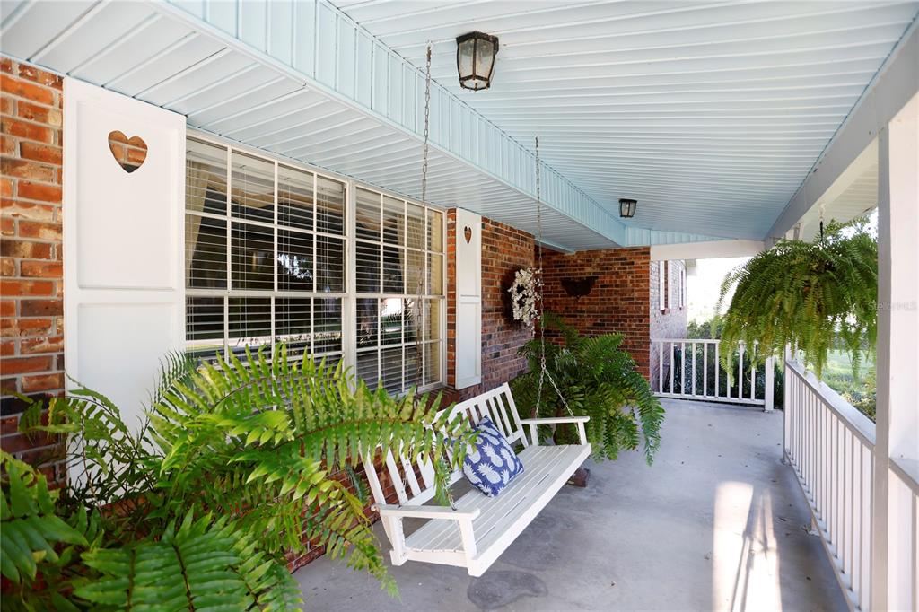 A covered brick porch features a white hanging bench, potted ferns, and light blue ceiling — 23378 EPPLEY DRIVE, BROOKSVILLE, FL