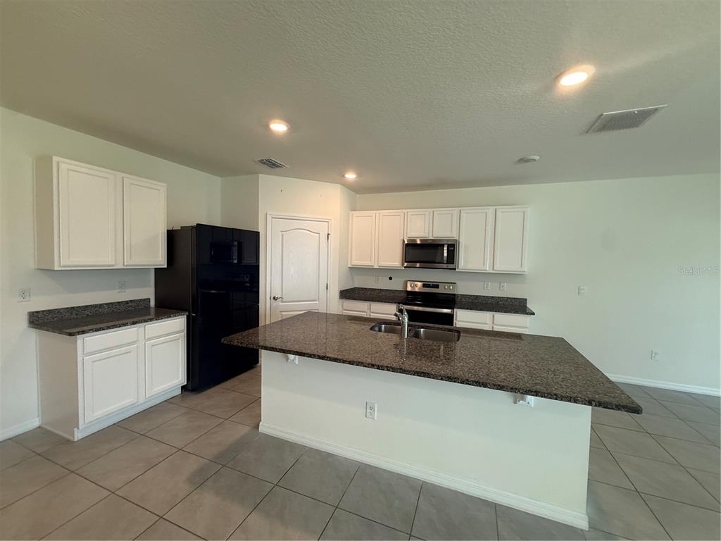 A kitchen features white cabinets, dark granite countertops, a black refrigerator, and tile flooring — 11106 AMBER RIDGE DRIVE, ZELLWOOD, FL
