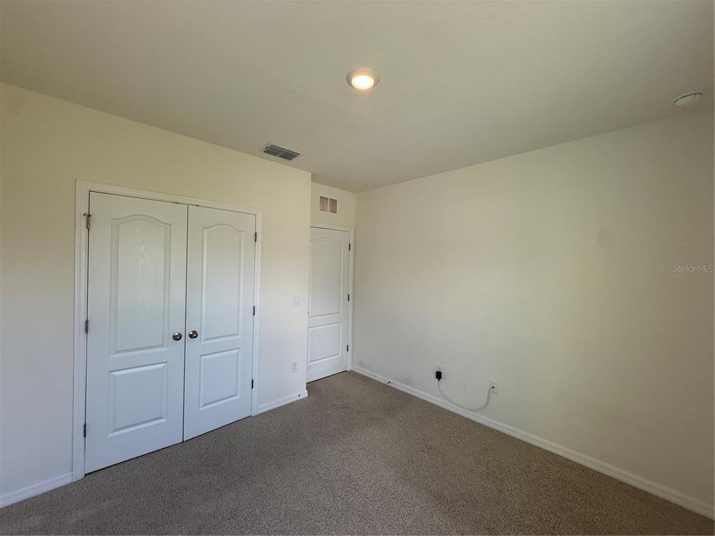 An empty bedroom features beige carpet, white walls, a double-door closet, and a single door — 11106 AMBER RIDGE DRIVE, ZELLWOOD, FL