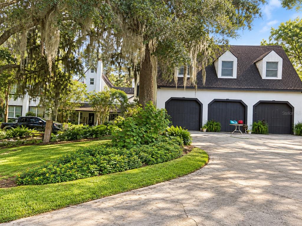 A white house with a three-car garage and a large tree in the front yard — 26307 MOUNTAIN LAKE ROAD, BROOKSVILLE, FL