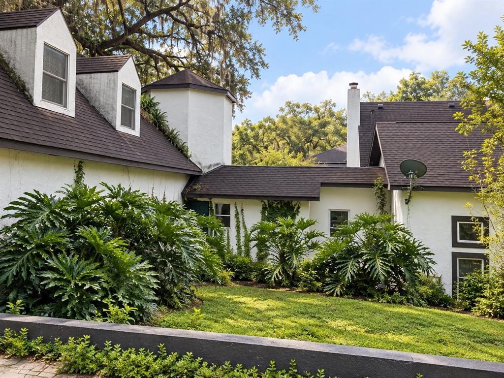 A white stucco house with a dark shingled roof and dormer windows sits behind landscaping — 26307 MOUNTAIN LAKE ROAD, BROOKSVILLE, FL
