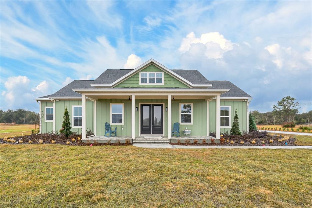 A single-story green house with a front porch and dark double doors under a cloudy sky — 38801 RANCH GATE BOULEVARD, UMATILLA, FL