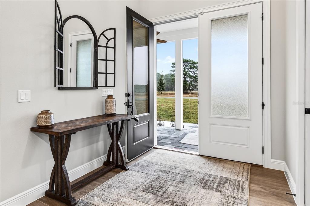An entryway features a wooden console table, a decorative mirror, and an open door to outdoors — 38801 RANCH GATE BOULEVARD, UMATILLA, FL
