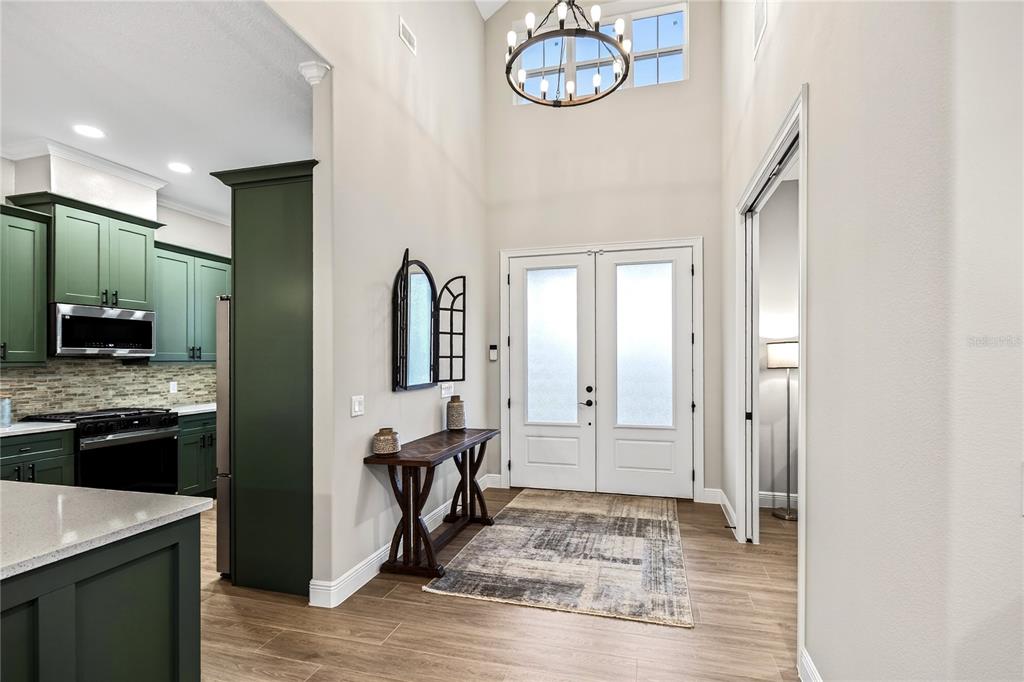 An entryway with a high ceiling, chandelier, double front doors, and an adjacent kitchen — 38801 RANCH GATE BOULEVARD, UMATILLA, FL