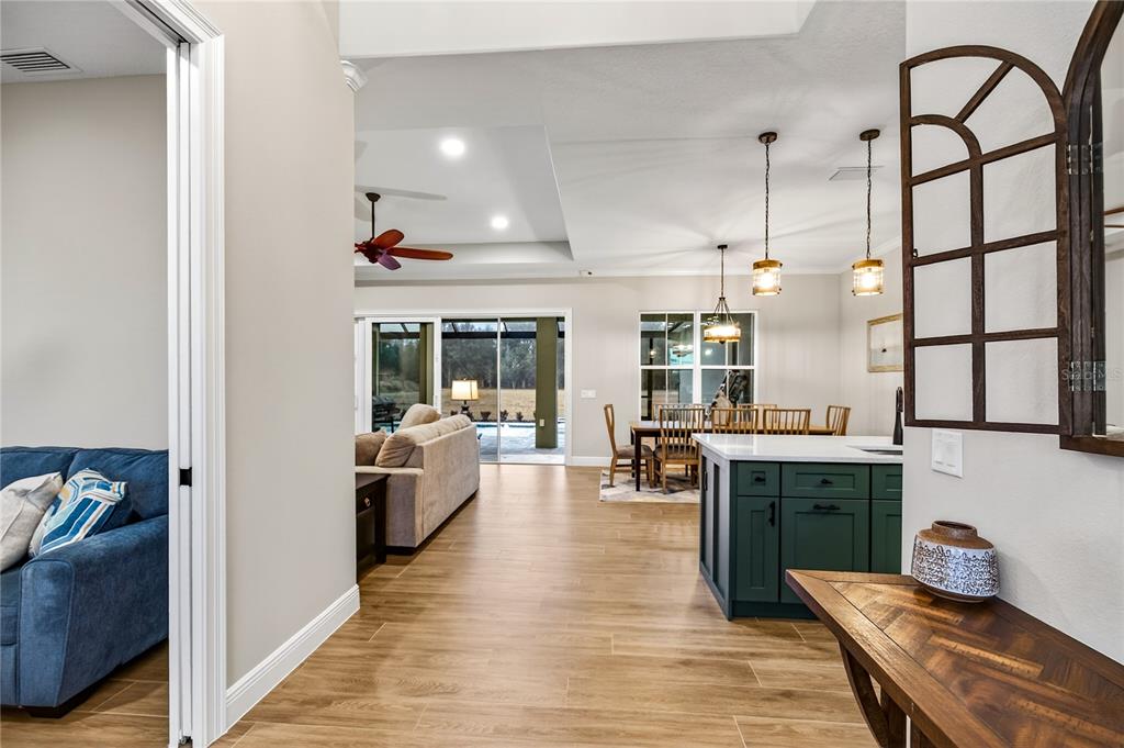 An open-concept living and dining area features wood-look tile floors and a green kitchen island — 38801 RANCH GATE BOULEVARD, UMATILLA, FL