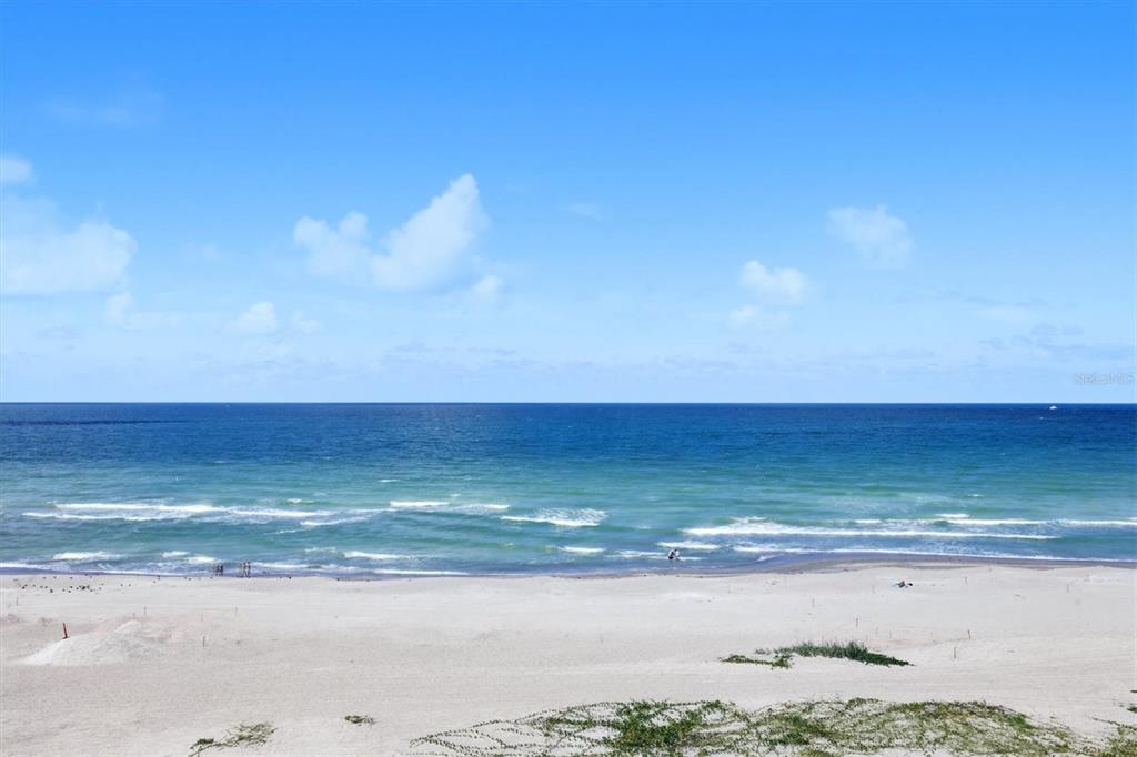A wide, elevated view of a sandy beach meeting the blue ocean under a clear sky — 255 THE ESPLANADE N UNIT 707, VENICE, FL