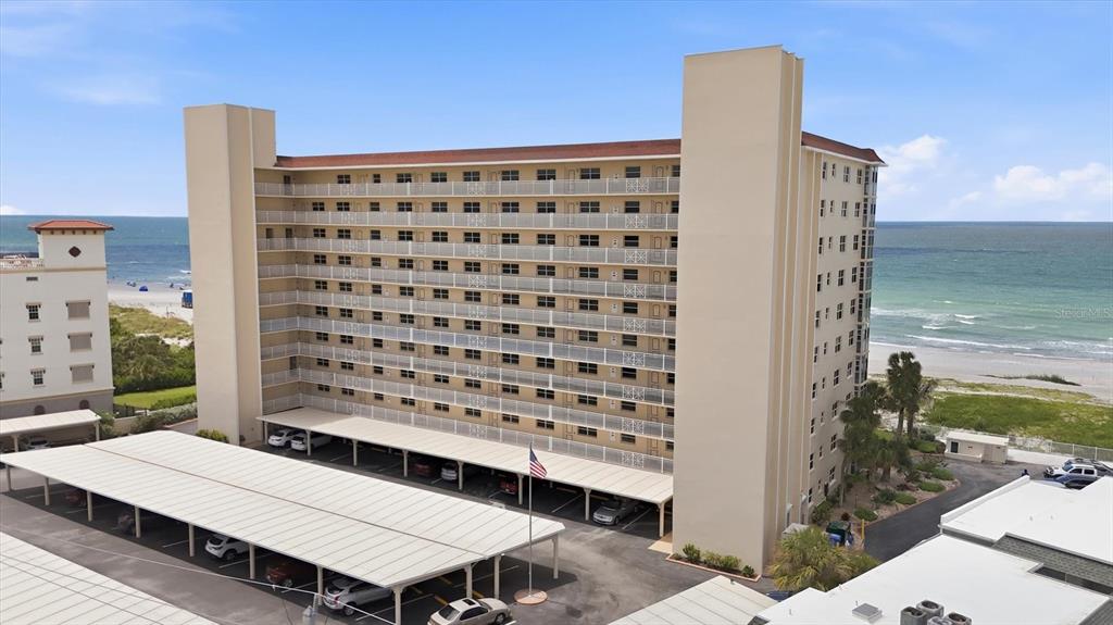 An aerial view shows a multi-story beachfront condominium building with covered parking and a flag pole — 255 THE ESPLANADE N UNIT 707, VENICE, FL