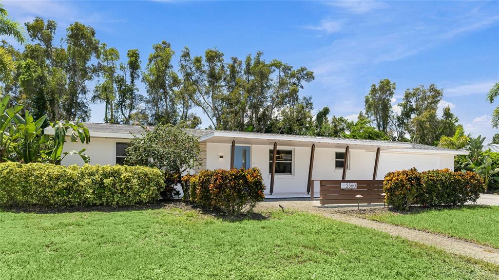 A single-story white house with a flat roof, covered porch, and landscaped front yard — 2560 SUNNYSIDE STREET, SARASOTA, FL