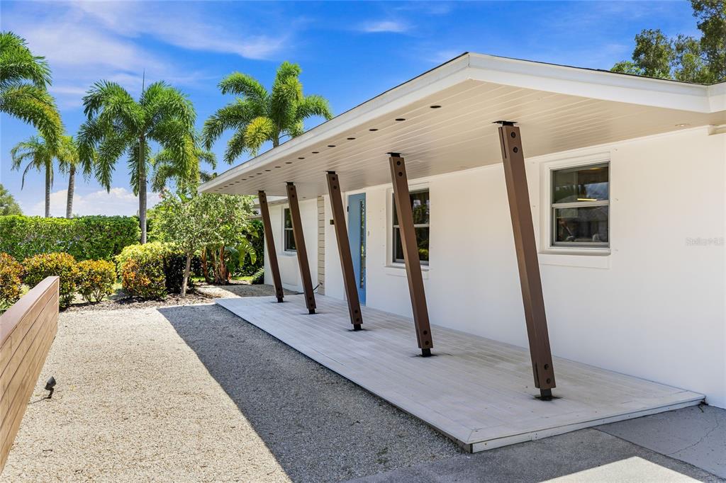 A white house exterior features a covered wooden porch supported by angled brown metal posts — 2560 SUNNYSIDE STREET, SARASOTA, FL